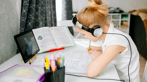 young girl studying online with tutor writing wearing black and silver headphones