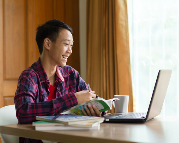 male student smiling working at laptop with coffee cup