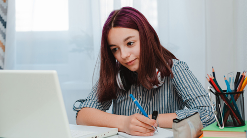 young student with purple hair and striped shirt writing and sitting on laptop