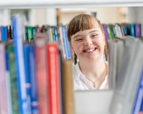 young student with disability smiling and browsing library books