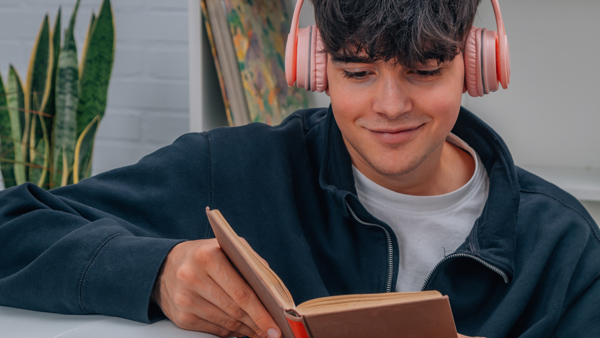 young male in pink headphones reading book