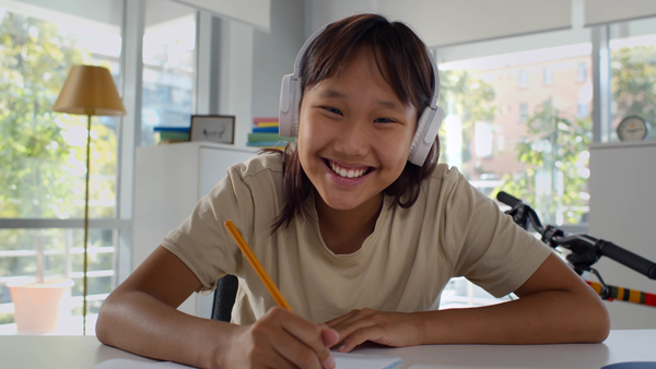young student smiling in white headphones holding yellow pen